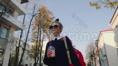一个漂亮的红包时髦少年在建筑物之间的一条塑料杯步行街上喝奶昔。可爱的女孩